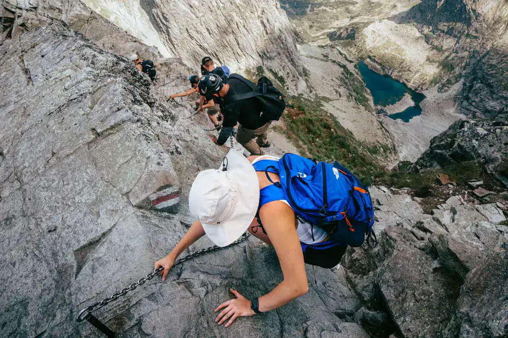 Group of hikers closely following a guide along a narrow rocky alpine ridge