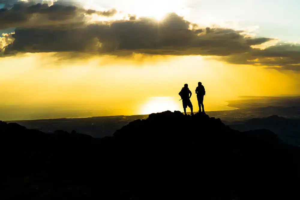 Hikers standing on a summit watching the sunset